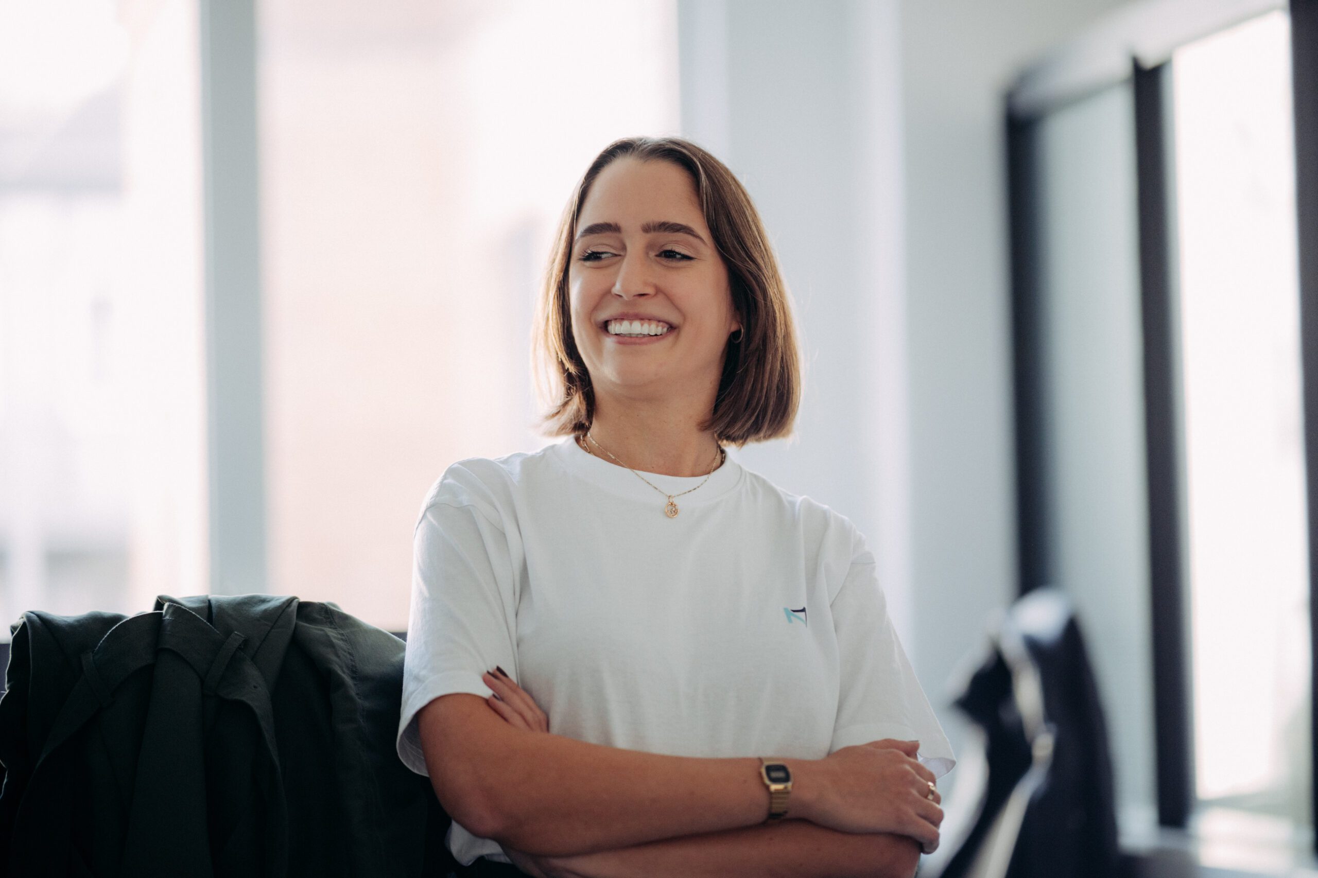 Eine Frau, die ein T-Shirt mit dem NEOMATIC Logo trägt, hat ihre Arme verschränkt und lächelt.