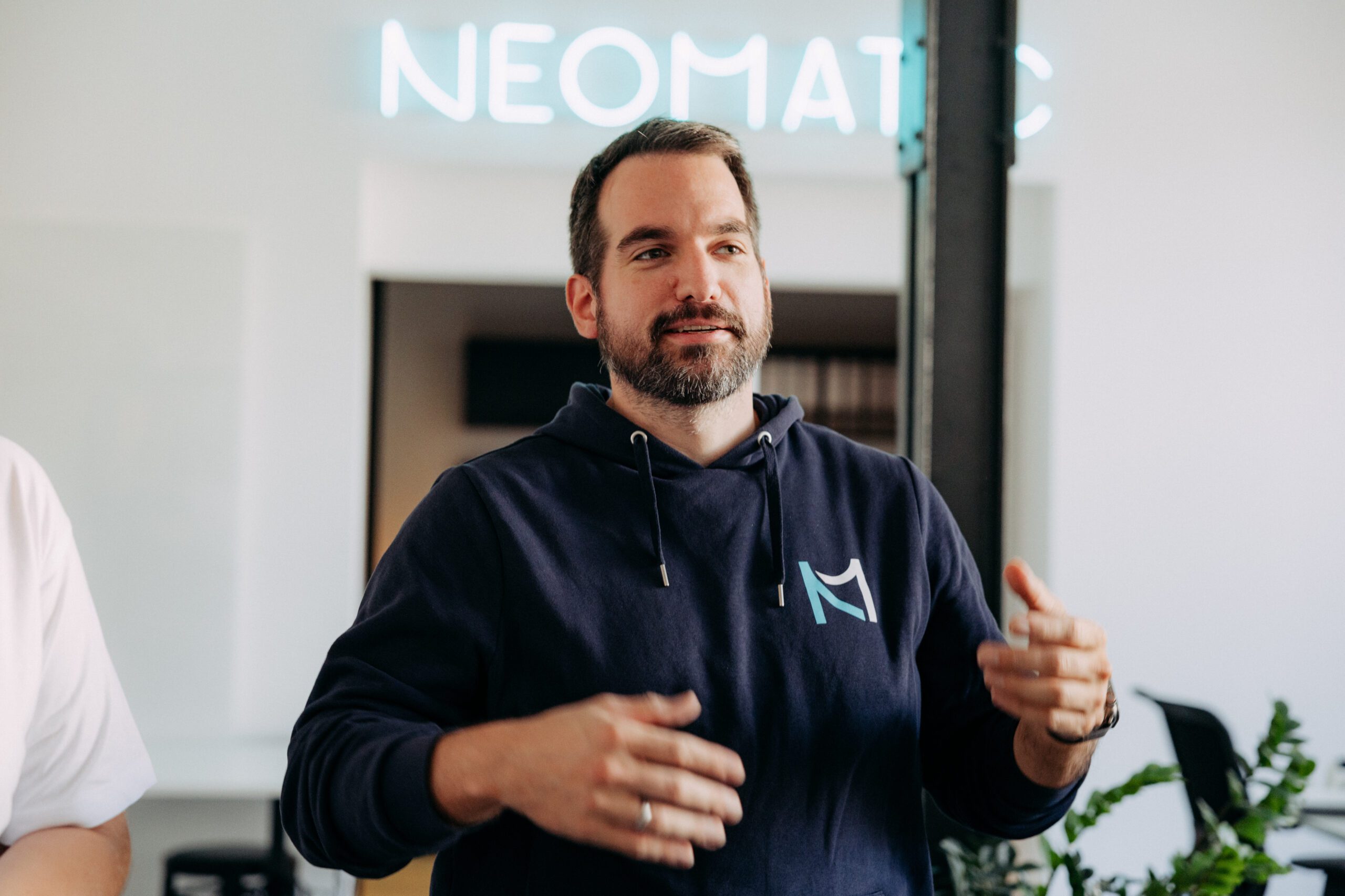Ein Mann, der einen NEOMATIC Pullover trägt, hebt seine Hände und blickt nach rechts im Bild.