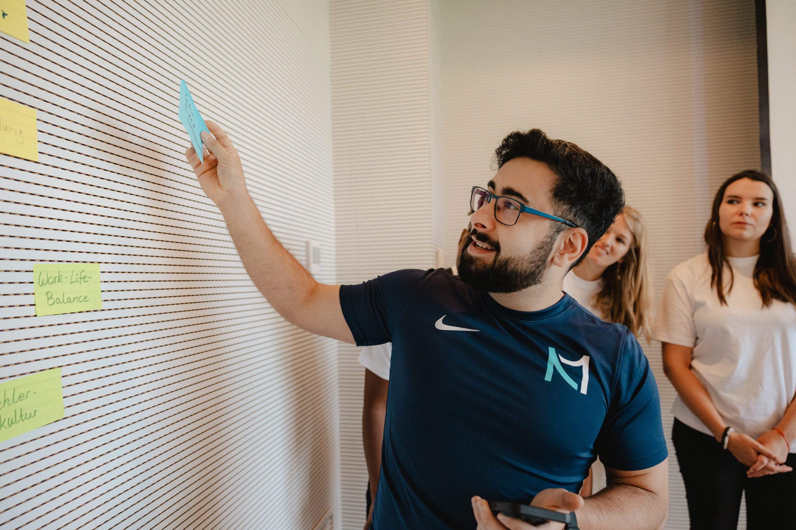 20240913_09_57_03-scaled Eine Person steht vor einer Wand und hält eine beschriftete Sticky Note.