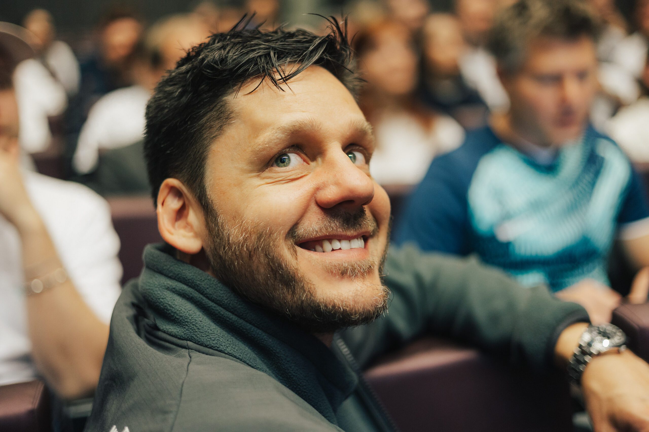 NEO.cation 2025 Ein Mann sitzt in einem Meetingraum und lacht mit dem Gesicht zur Kamera gedreht